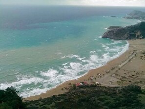 A coastal landscape with a beach, waves, and a distant view of the sea.