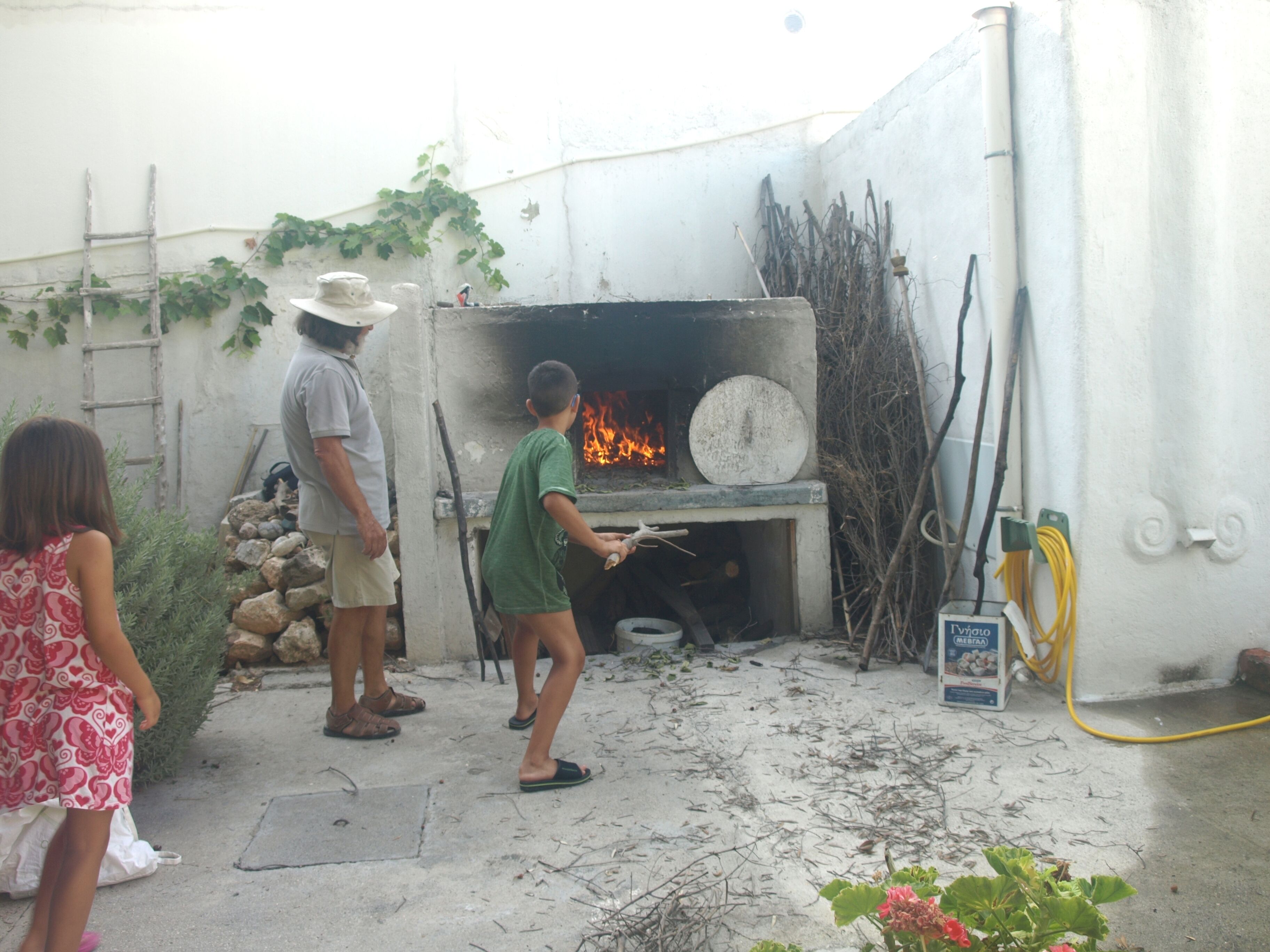 Un grupo de personas cerca de un horno de leña tradicional, con una escalera y algunas plantas por ahí.
