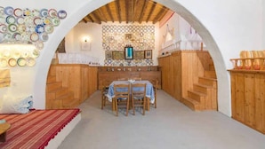 Un interior rústico con una mesa y sillas de madera bajo un techo abovedado, rodeado de paredes de madera y un adorno mural con diseño.