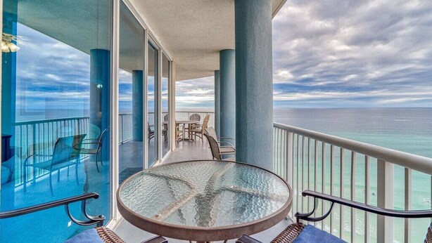 A balcony with a glass table and chairs, overlooking the ocean.