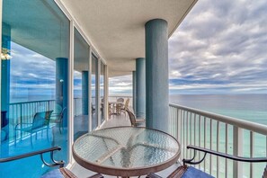 A balcony with a glass table and chairs, overlooking the ocean.