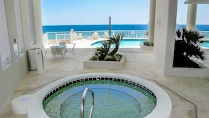 An indoor swimming pool with a view of the ocean, surrounded by lounge chairs and a small garden area.
