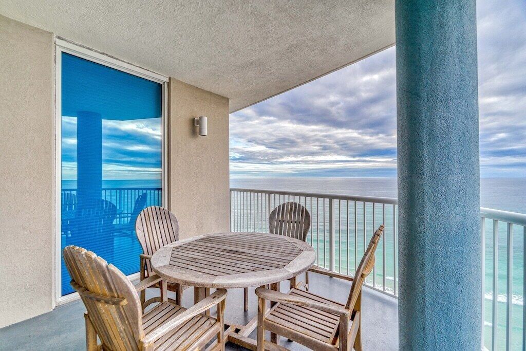 Un balcon avec une table ronde en bois et quatre chaises, donnant sur une étendue d’eau.