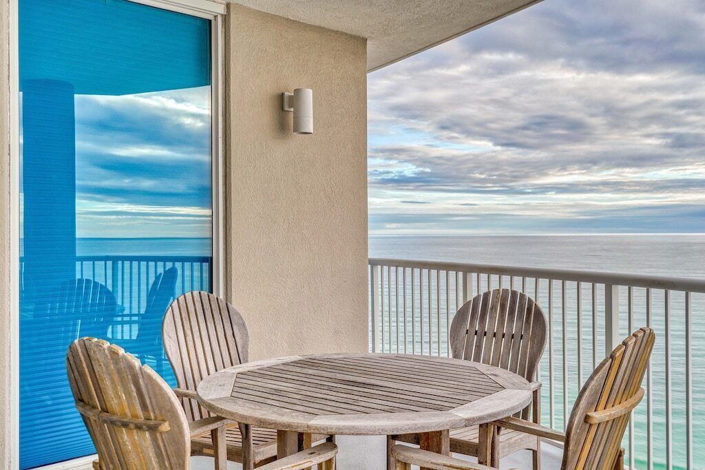 A round wooden table with four chairs on a balcony with a view of the ocean.
