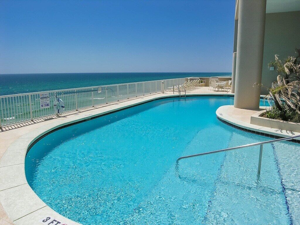 A clear blue pool with a 3 FT depth marking, surrounded by a white railing, with a view of the ocean.