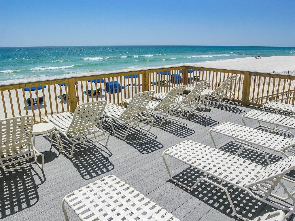 Une terrasse au bord de la plage, dotée de chaises longues et de tables, avec vue sur l’océan.