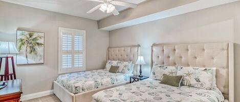 A bedroom with two beds, a ceiling fan, a desk, and a window with blinds.