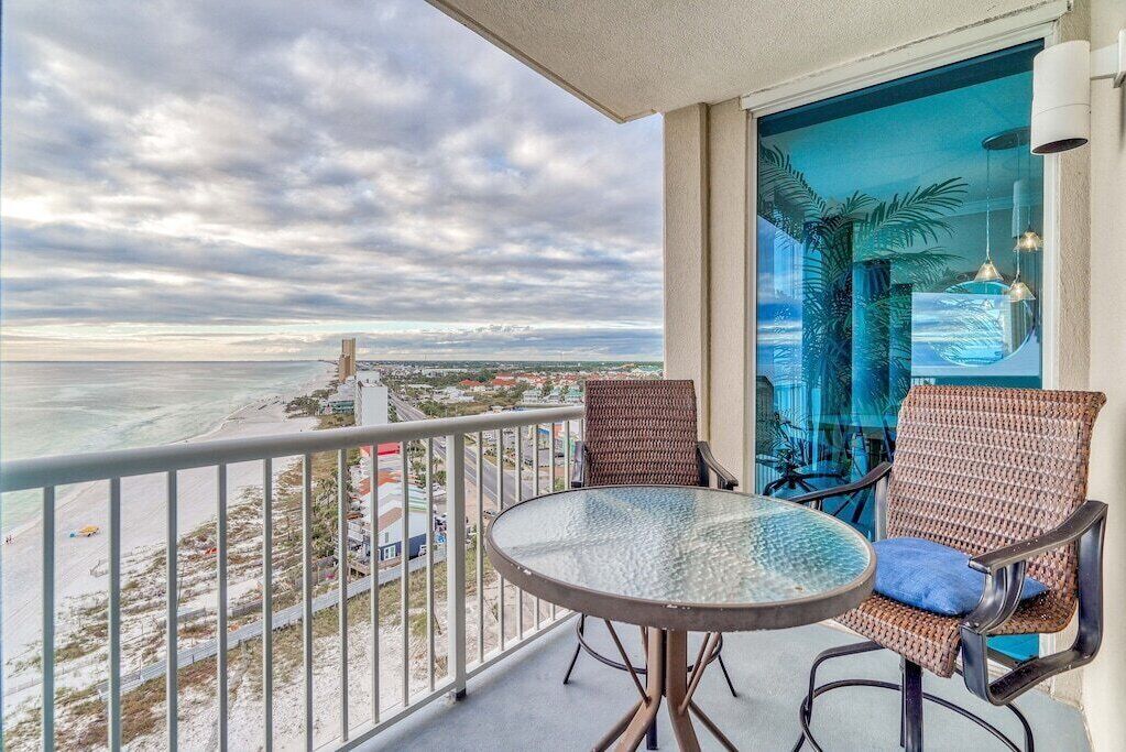 Un balcone con un tavolo in vetro e sedie in vimini, con vista su una spiaggia e sulla città.