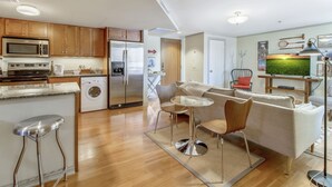 Uma cozinha moderna com eletrodomésticos de aço inoxidável, um espaço de refeições com uma mesa redonda e cadeiras, e uma sala de estar com sofá e televisão.