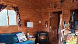 Un acogedor interior de cabaña con sofá, una mesita, una silla, chimenea y televisión.
