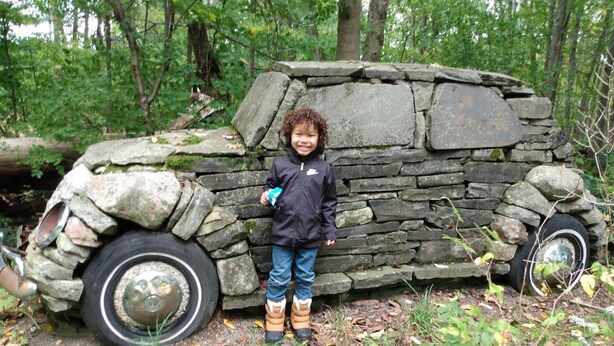 Un niño de pie junto a una estructura de piedra que parece un vehículo.