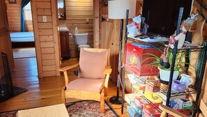 Interior acogedor de una cabaña de madera con una escalera de madera, un comedor con mesa y sillas, y un televisor en un estante.