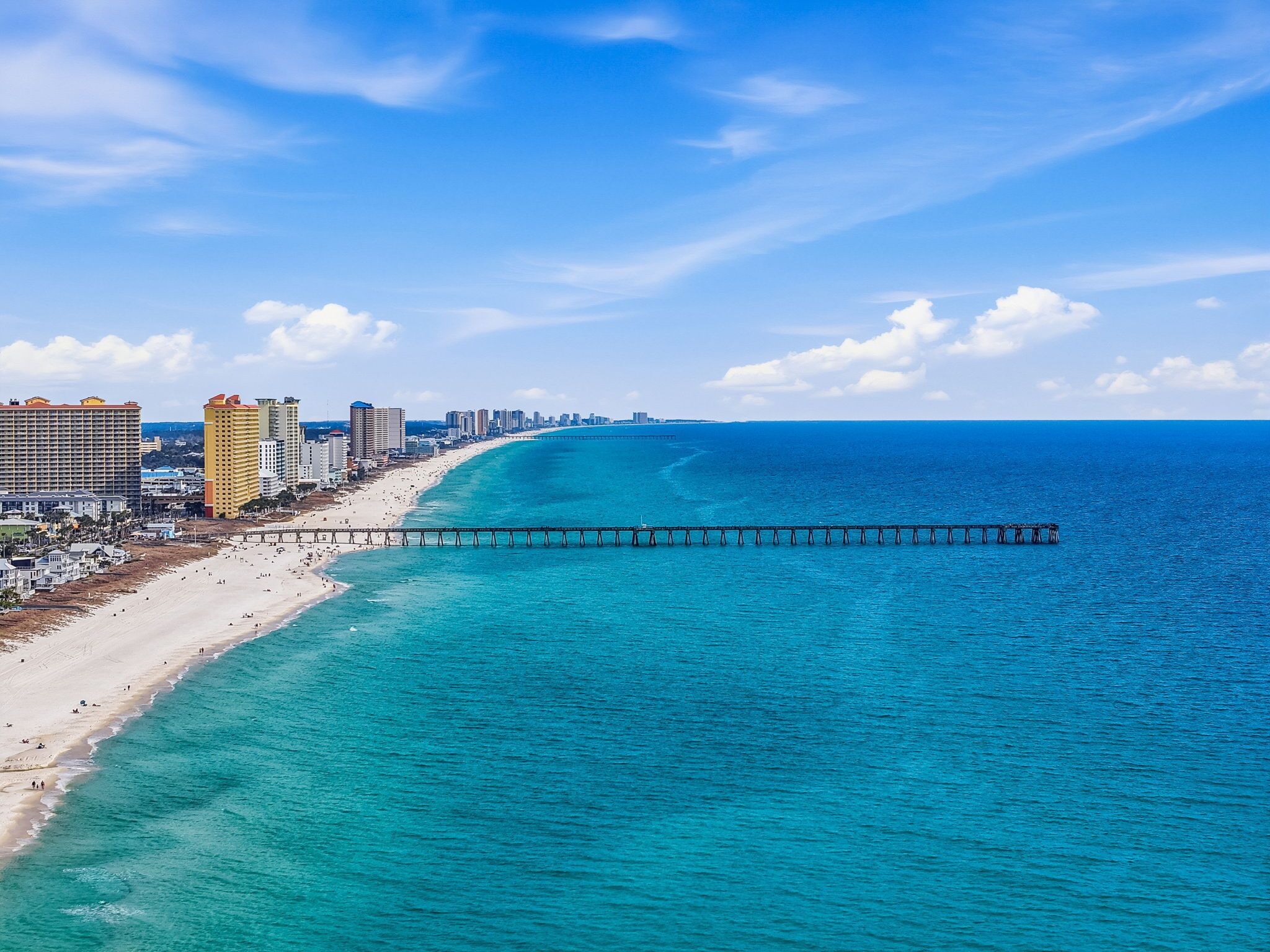 A coastal cityscape with a beach, a pier, and high-rise buildings.