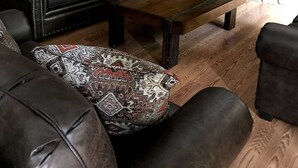 Una sala de estar acogedora con un sofá de cuero, cojines estampados, una mesa de centro de madera, chimenea y pared de piedra.