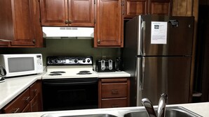 Cocina con gabinetes de madera, refrigerador de acero inoxidable, microondas, estufa y pileta con grifos modernos.