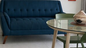 A modern living room with a blue sofa, a glass table, a ceiling fan, and a city view. - Amazing, OCEAN VIEW STUDIO - BALCONY- Wi-Fi -APT has GENERATOR- PARKING Optional (Condado, San Juan)