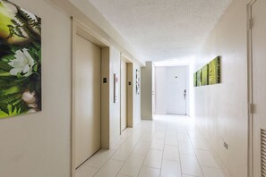 A hallway with white walls, a tiled floor, and doors leading to rooms. There are framed pictures on the walls and a door with a keyhole.