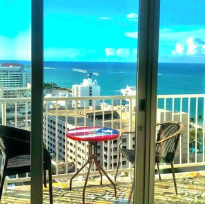 A balcony with a table and chairs, overlooking a cityscape and the ocean.