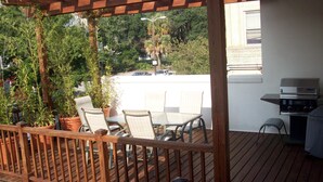 Una terraza de madera con pérgola, mobiliario exterior y una parrilla.