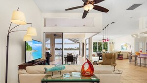 A spacious living area with a television, a ceiling fan, and a glass coffee table. - Beautiful Villa Lake View Heated Pool, Salt💧Spa & Kayak’s🐠 Simply Wonderful! (Cape Coral)