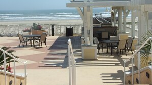 Un patio frente a la playa con mobiliario exterior, una pérgola y vistas al océano.