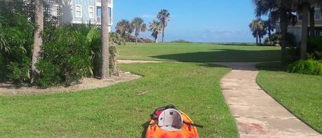A kayak on a grassy path with a building and palm trees in the background.