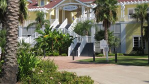 Un resort con una escalera central que conduce a un área techada, palmeras y un letrero que indica el Beach Club.