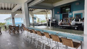 Una zona de bar con barra, taburetes y vistas al océano.