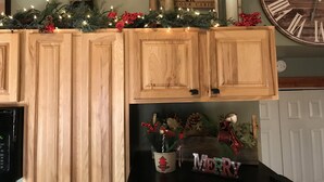 Una cocina con armarios de madera, un reloj y decoraciones navideñas, incluyendo un letrero que dice 'Merry' y uno con la palabra 'Welcome'.