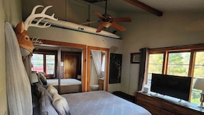 Un dormitorio con una cama grande, un ventilador de techo, un televisor montado y una decoración con cabeza de venado.