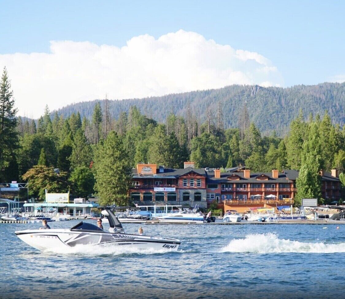 Un hôtel situé au bord de l’eau, composé de plusieurs bâtiments, avec des bateaux amarrés et une montagne boisée en toile de fond.