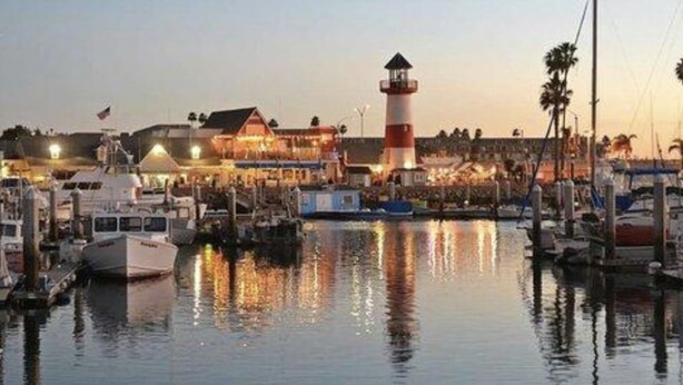 A marina with boats docked, a lighthouse, and a building with lights on. - Private Enchanted Garden (Oceanside)