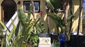 A patio area with a stone table, a blue vase, and a wicker chair with a cushion. - Private Enchanted Garden (Oceanside)