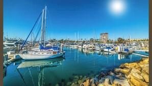 A marina with multiple boats docked, a clear sky, and a building in the background. - Private Enchanted Garden (Oceanside)