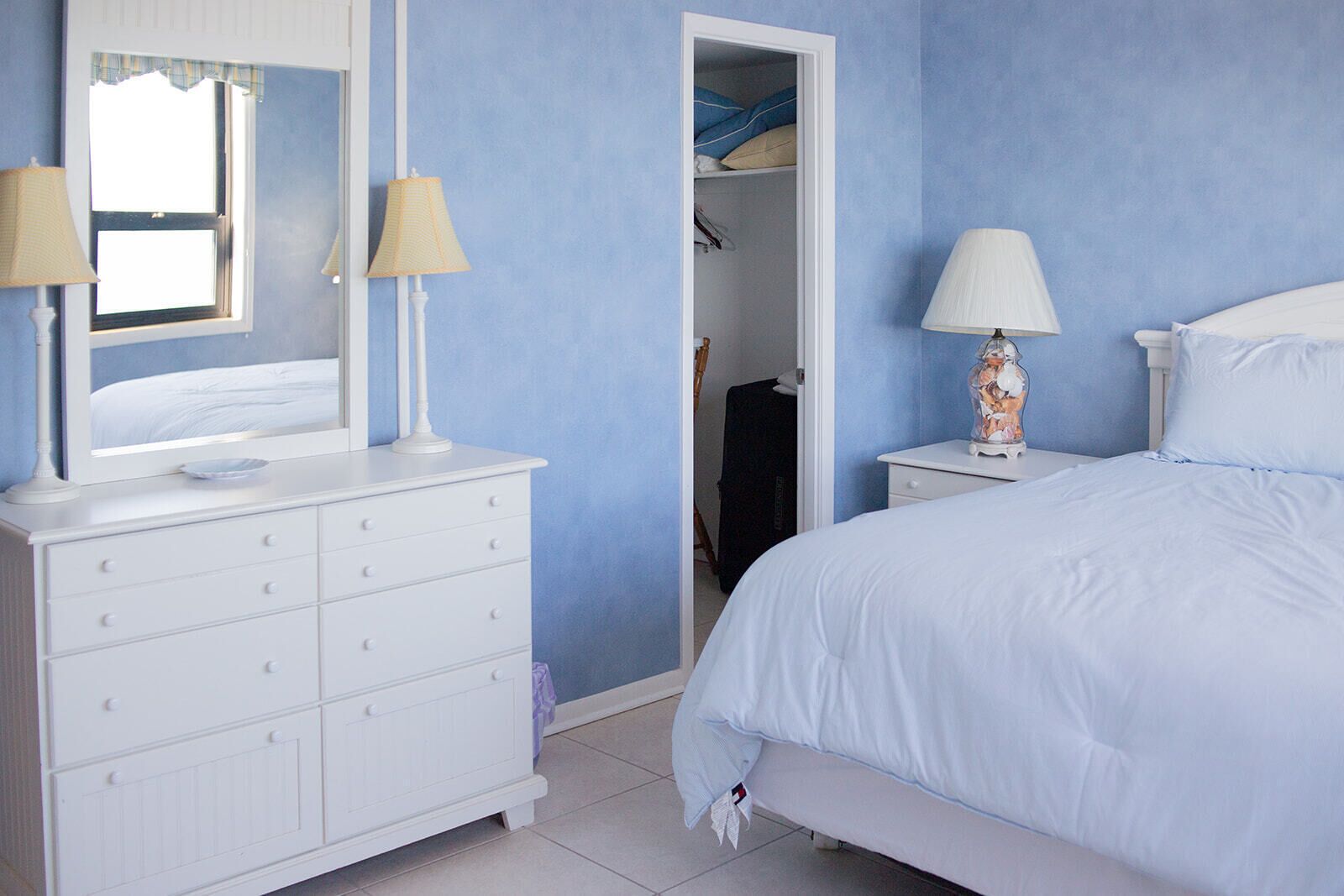 A bedroom with a bed, a dresser, two lamps, and a mirror.