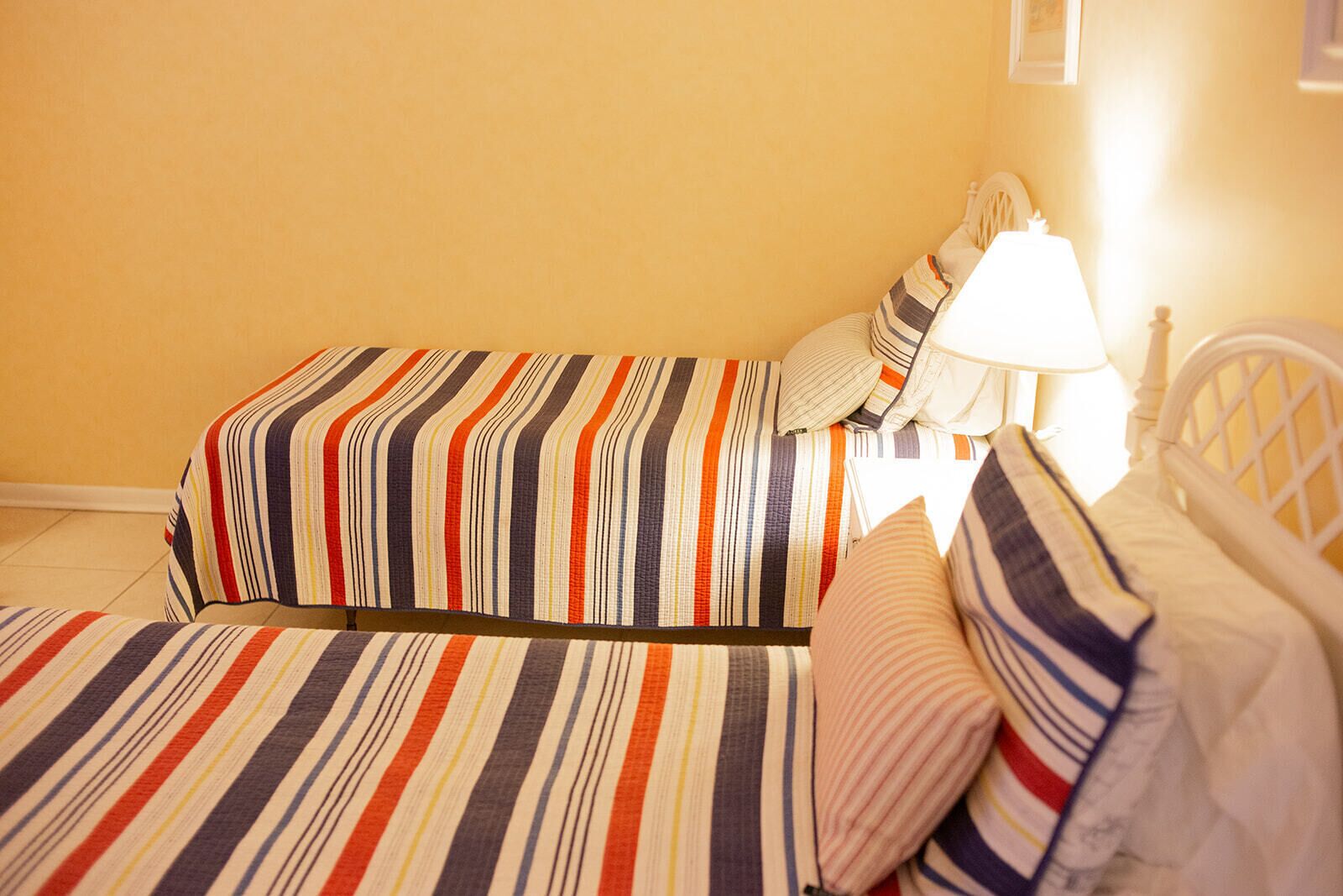 Une chambre avec deux lits, chacun doté d’une literie et de coussins à rayures, d’une tête de lit blanche et d’une lampe de chevet.