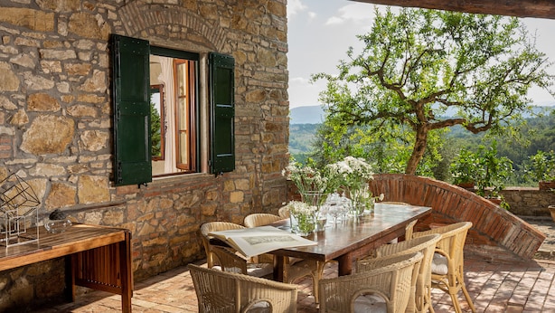 A stone building with a wooden table and wicker chairs, overlooking a lush landscape. - LaQuerciaEstate -Quintessential Italian Experience (Impruneta)