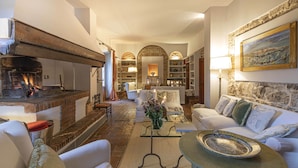 A cozy living room with a fireplace, a stone wall, and a view of the kitchen. - LaQuerciaEstate -Quintessential Italian Experience (Impruneta)