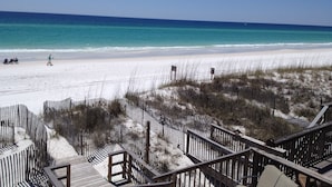 A beach with a wooden boardwalk leading to the shore, clear blue water, and a sandy beach.