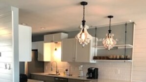 A modern kitchen with a central island, bar stools, pendant lighting, and white cabinetry.