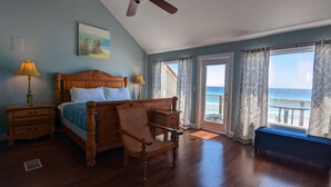 A bedroom with a wooden bed, two bedside tables with lamps, a bench, and a view of the ocean through large windows.