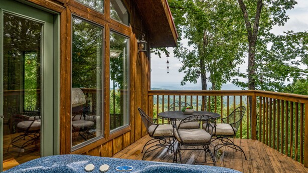 Eine Holzterrasse mit Whirlpool, Sitzgelegenheiten im Freien und Blick auf Bäume und Berge.