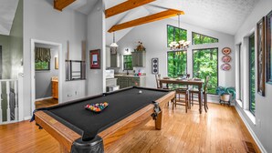 Ein geräumiger Raum mit Poolbillard, Holzbalken, großen Fenstern und einem Essbereich.