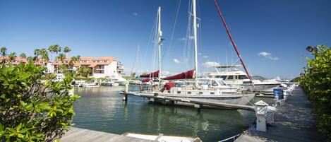 A marina with boats docked, a wooden dock, and a building with a red roof in the background.