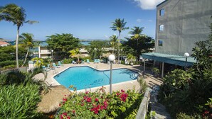 A pool area with lounge chairs, palm trees, and a view of the ocean.