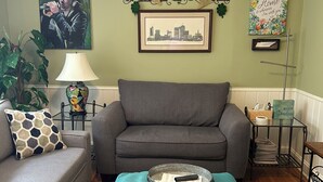 A living room with a grey sofa, teal pouf, and a cityscape picture on the wall. - 5* Cutie Has It All! Just Bring Family & Friends! (Nashville)