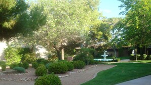A landscaped garden with a fountain, trimmed bushes, and a paved walkway. - Great Deck for Spectacular Sunrises in Sports Village (St George)