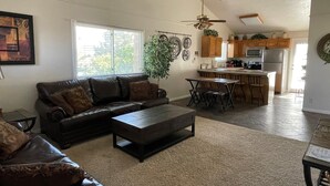 A living room with a sofa, coffee table, and a dining area with chairs. There is a kitchen in the background with cabinets and appliances. - Great Deck for Spectacular Sunrises in Sports Village (St George)