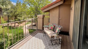 A balcony with a cushioned seating area, a metal railing, and a view of a landscaped garden and trees. - Great Deck for Spectacular Sunrises in Sports Village (St George)