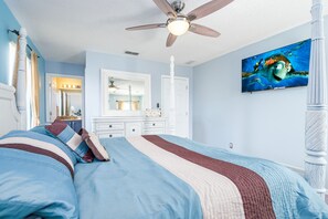 A bedroom with a bed, a ceiling fan, a dresser, a mirror, and a painting on the wall.